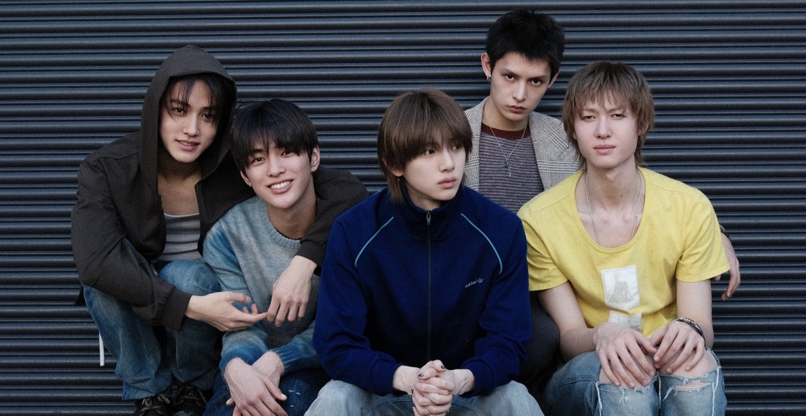 The five members of CORTIS crouched in front of a metal shutter