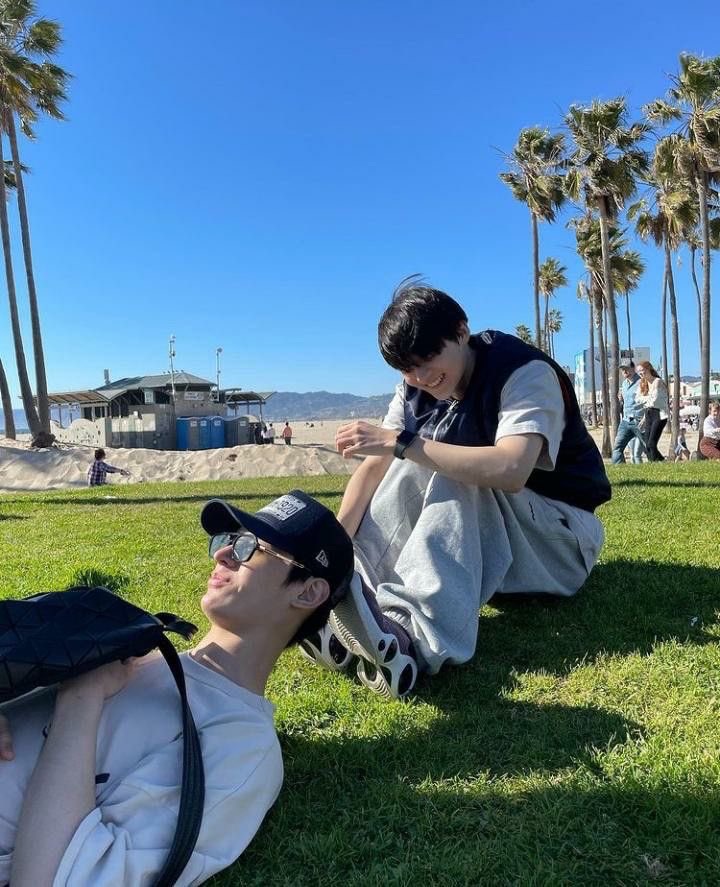 James and Sangwon of Trainee A sitting on the grass under palm trees in Los Angeles