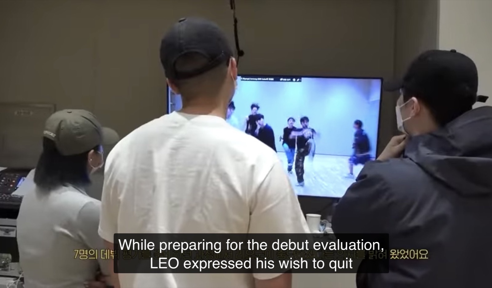 Staff watching a Trainee A performance on a monitor, with a subtitle saying Leo expressed his wish to quit while preparing for the debut evaluation